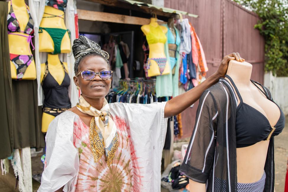 Bernadette stands in front of her business in Cameroon established with support from IOM after returning from Libya. Photo: Credit IOM/ Beyond Borders Media 2022