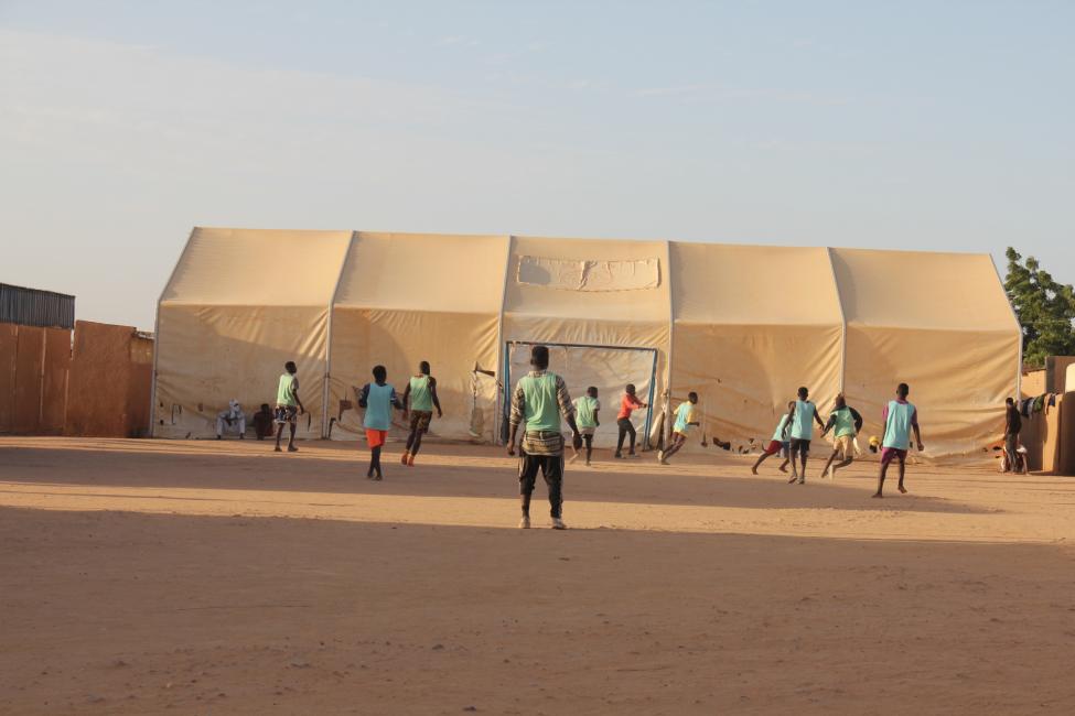 Migrants playing football at one of IOM’s seven transit centres in Niger where close to 5,000 people receive essential services. Amidst the current political instability, humanitarian corridors must be established to allow migrants to return home in a safe and dignified manner. Photo: IOM/Souleymane Galadima